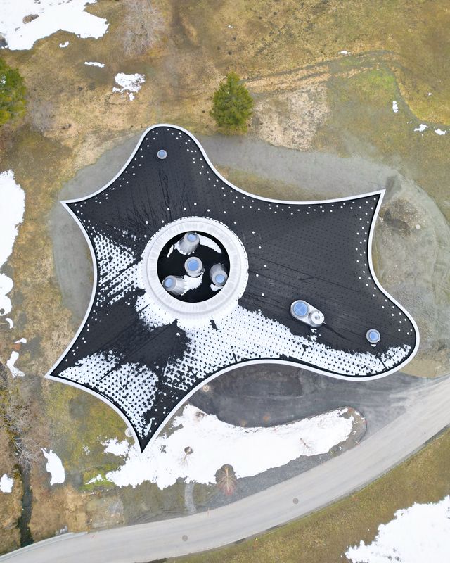 Klanghaus Toggenburg am Schwendisee – Luftaufnahme der fertigen Dachaufsicht aus EPDM-Bahnen samt Klemmhaltern und Pfannendeckeln. Der verblechte Dachkranz beherbergt die Abluft sowohl der natürlichen Lüftung als auch der Hinterlüftung der Dachkonstruktion und fasst die vier Oblichtkegel ein. – Roland Bernath